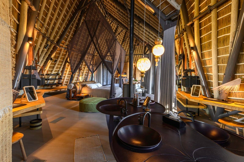 Elevated luxury safari lodge with wooden walkways connecting thatched-roof suites above wetlands in Botswana's Okavango Delta