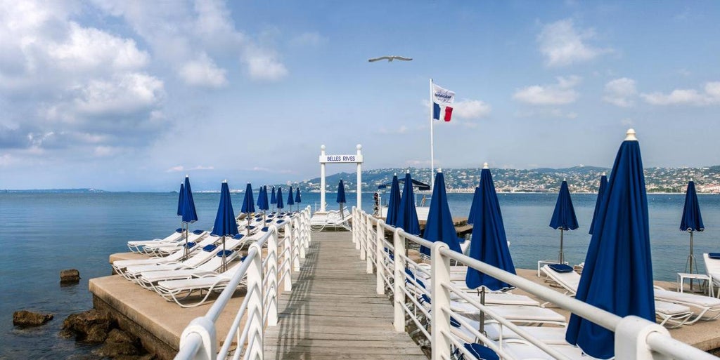 Elegant Art Deco hotel Belles Rives on French Riviera with private beach pier, blue Mediterranean waters and manicured garden terrace