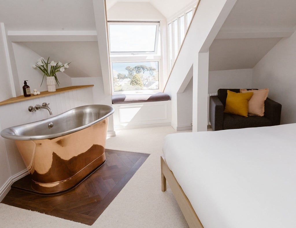 Elegant coastal-inspired bedroom with crisp white linens, plush throw pillows, and expansive sea view window in The Sandy Duck boutique hotel room