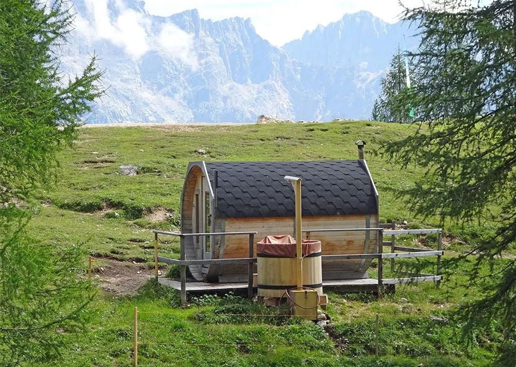 Historic mountain lodge with wooden balconies nestled in Italian Dolomites, surrounded by dramatic rocky peaks and alpine meadows