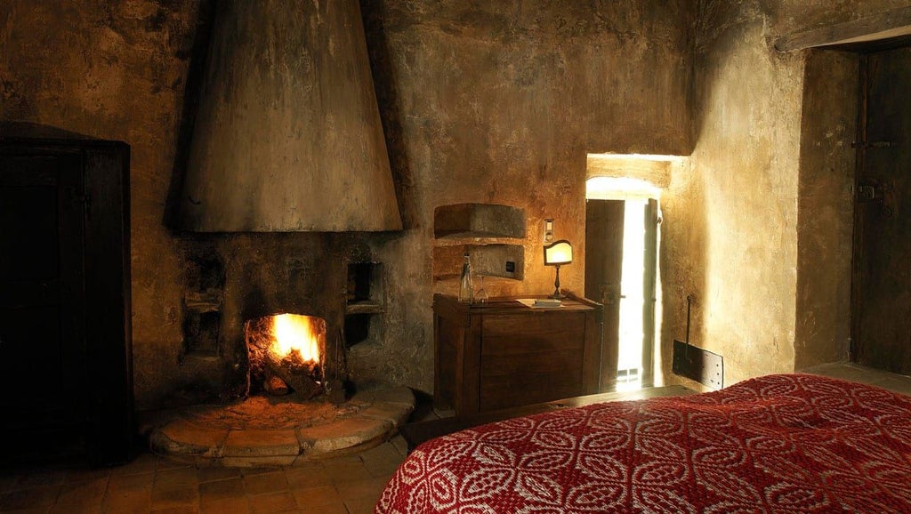 Rustic stone interior of historic Italian hotel room with minimalist wooden bed, traditional stone walls, and warm ambient lighting in Santo Stefano di Sessanio