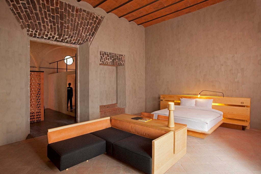 Luxurious downtown Mexico Revolution Suite with modern king bed, exposed brick walls, urban artwork, and panoramic city skyline through large windows