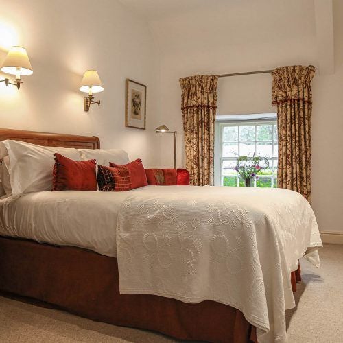 Elegant classic hotel room with plush cream bedding, antique wooden furniture, soft ambient lighting, and refined pastoral decor at luxurious UK country estate