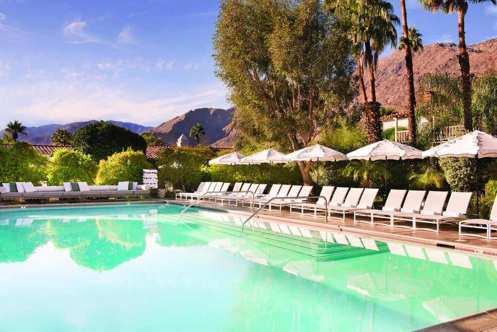 Mediterranean-style luxury hotel facade with white stucco walls, elegant archways, and towering palm trees in Palm Springs' golden sunlight