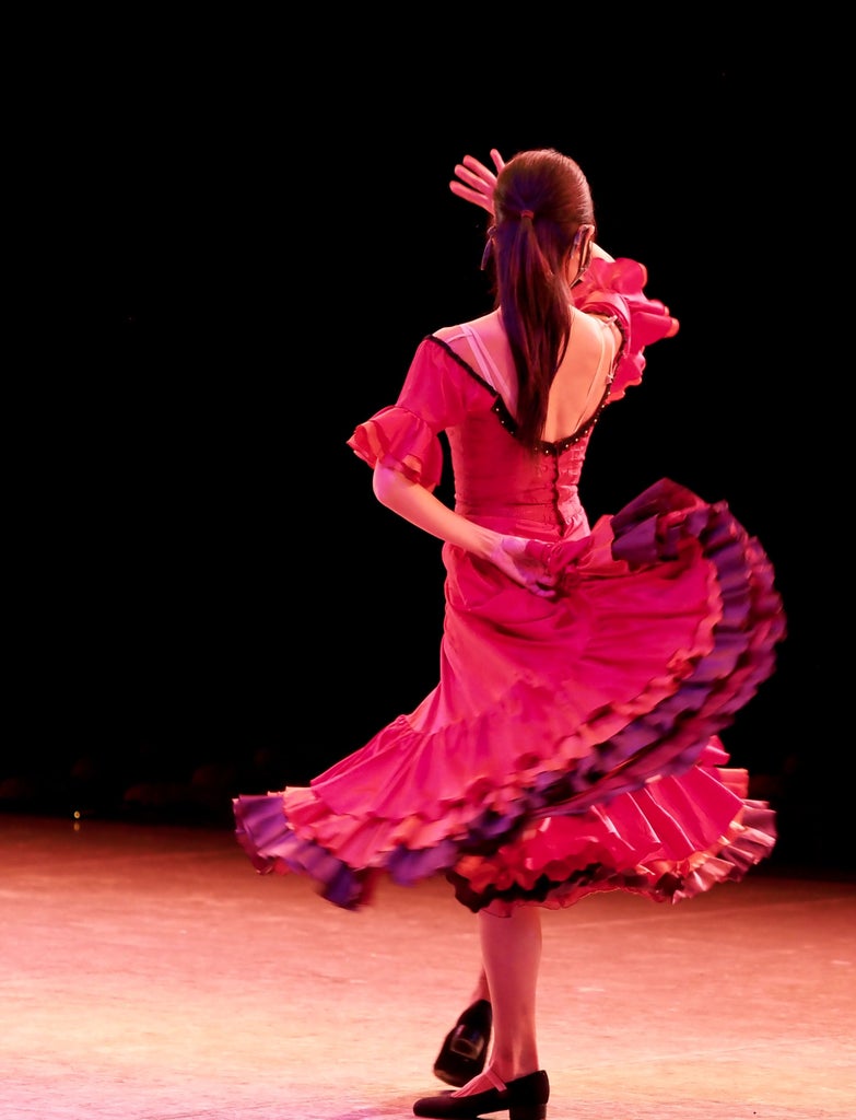 Female flamenco dancer performing in ornate theatre, wearing red ruffled dress, dramatic pose with arms raised against golden stage lighting