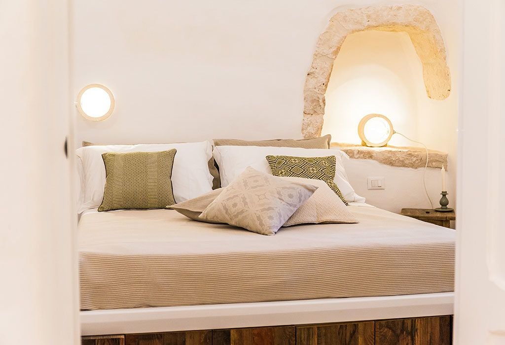 Luxury stone-walled suite with rustic charm, featuring a plush white bed, arched windows, and elegant traditional Italian design elements in Puglia