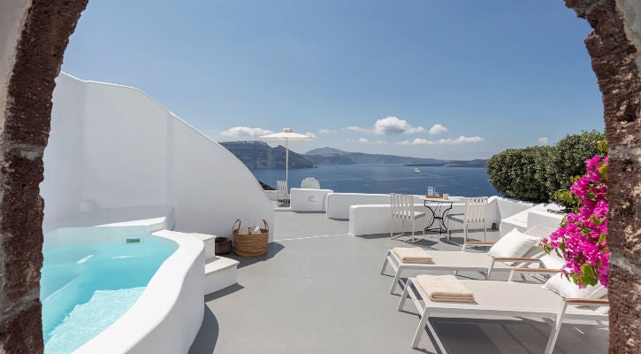 Whitewashed cliffside suites with private infinity pools overlooking Santorini's caldera and Aegean Sea at sunset