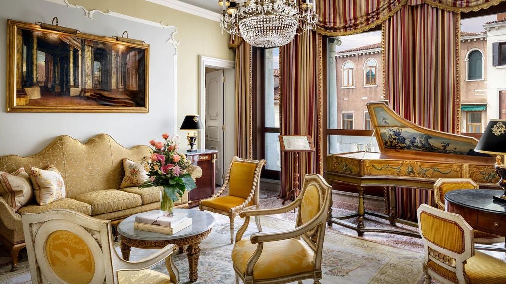 Opulent Venetian suite with ornate gold-framed mirrors, crystal chandelier, antique furniture, and silk-draped windows overlooking canal views