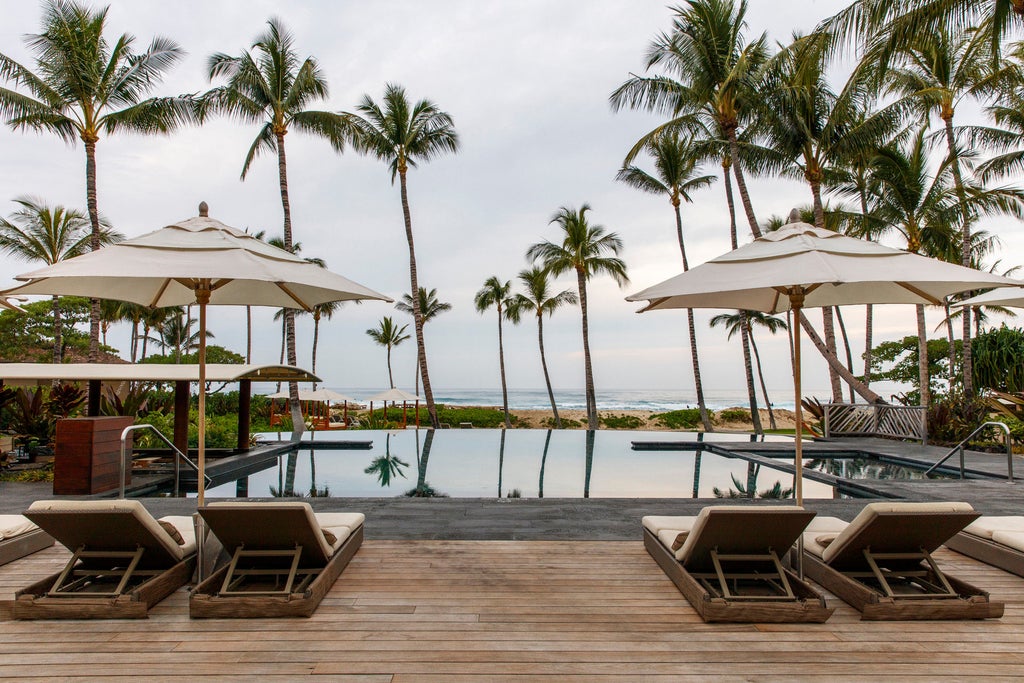 Oceanfront luxury resort with infinity pool overlooking Pacific Ocean, palm trees and tropical gardens at sunset in Hawaii