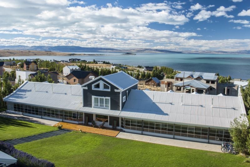 Large stone and wood luxury lodge nestled in snow-capped Andes mountains, with panoramic windows overlooking serene alpine lake