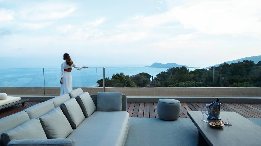 Infinity pool overlooking Mediterranean coastline, modern white villa with panoramic terrace, surrounded by manicured gardens at sunset