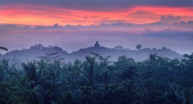 Infinity pool overlooking Borobudur temple and lush mountains with luxury poolside loungers amid tropical landscaping at sunset