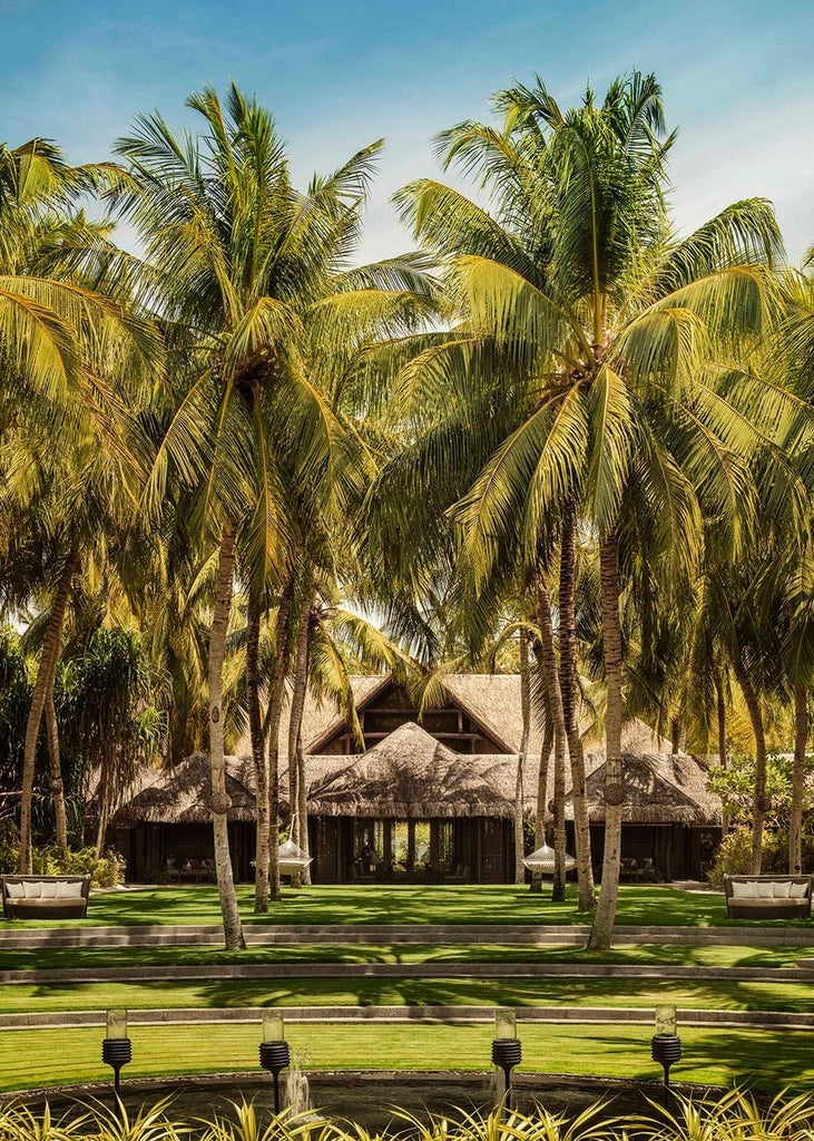 Luxurious overwater villa with private infinity pool extending into crystal-clear Maldivian lagoon, surrounded by palm trees at sunset