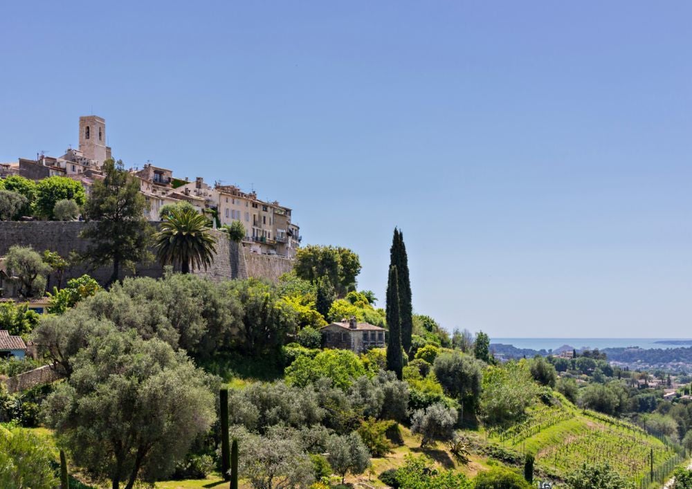 Elegant French boutique hotel facade with stone walls, traditional blue shutters, and charming window boxes with vibrant flowers in Saint-Paul-de-Vence