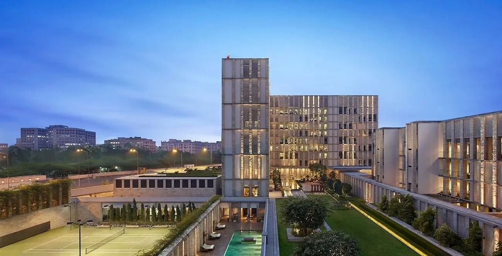 Contemporary Indian luxury hotel with geometric facade, infinity pool reflections, and manicured gardens under soft evening light