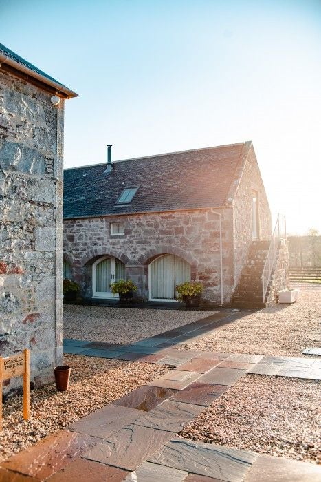 Spacious luxury family cottage in scenic United Kingdom countryside, featuring grand red gates, traditional stone exterior, and elegant landscaped surroundings at Newhall Mains estate