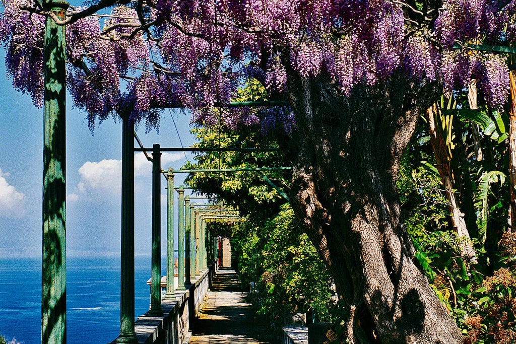 Historic luxury Italian hotel with ornate facade, stone balconies, and manicured gardens overlooking the Mediterranean Sea at sunset