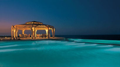 Elegant beachfront resort with palm-fringed pools, white Mediterranean architecture, and Red Sea views from private terraces at sunset