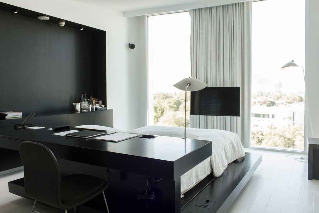 Modern minimalist hotel room with sleek gray furnishings, floor-to-ceiling windows, and contemporary design highlighting elegant urban luxury in Monterrey, Mexico.