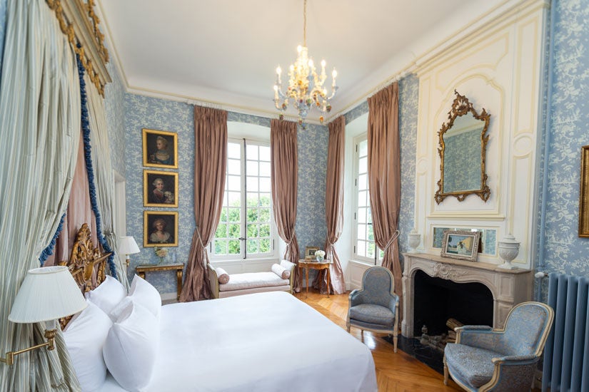 Elegant corner king room with crystal chandelier, gilded mirrors, French doors and garden views in an 18th-century Loire Valley château