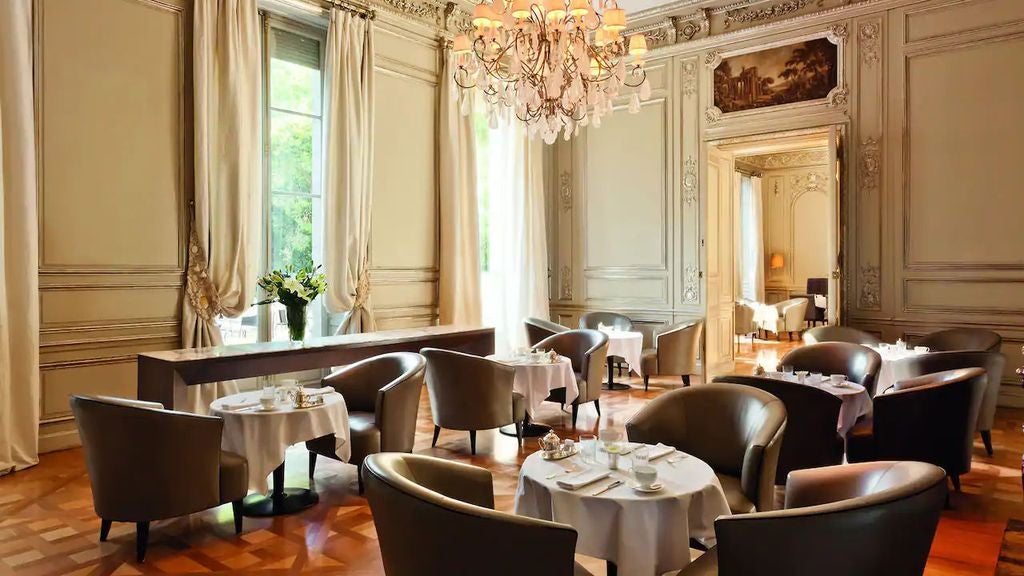 Elegant neoclassical palace hotel with white stone facade, ornate columns and archways, overlooking manicured French gardens in Buenos Aires