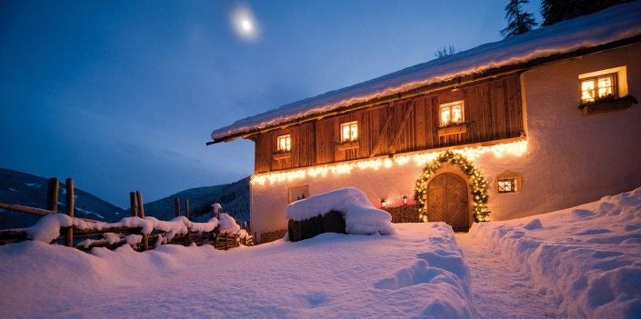 Rustic-luxe mountain lodge with wooden facade nestled in Italian Alps, featuring panoramic valley views and snow-capped peaks backdrop