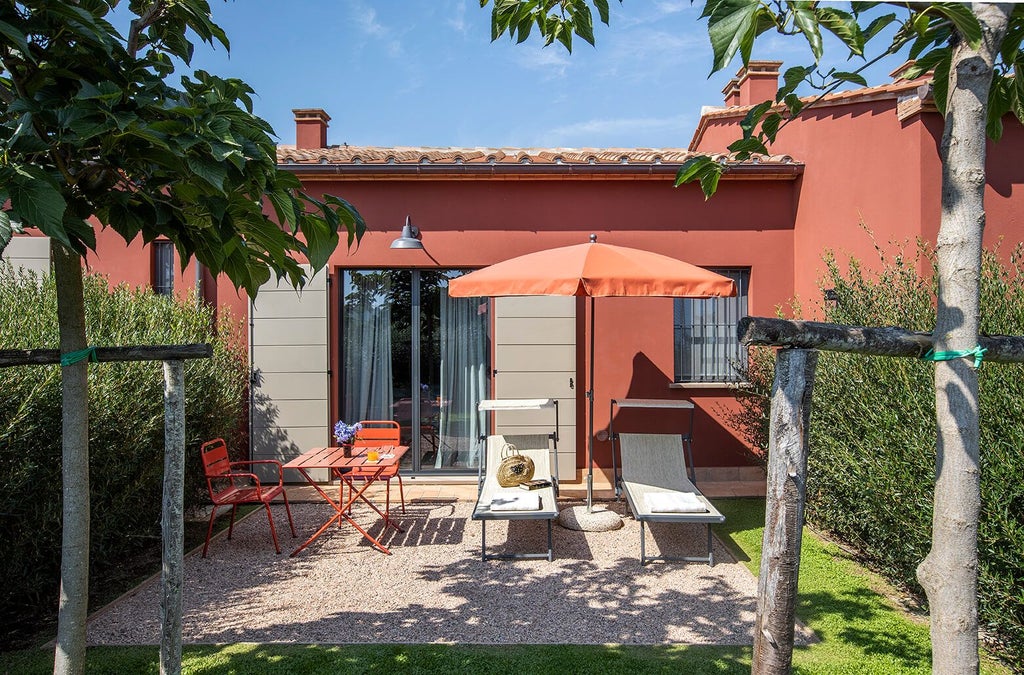 Elegant Tuscan garden suite with rustic stone walls, plush white bed, and expansive windows overlooking lush green Italian countryside landscape