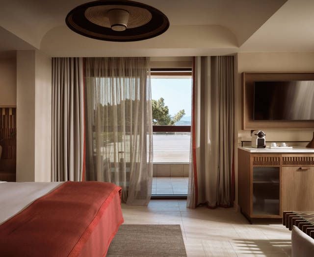 Elegant deluxe junior suite at Eagles Palace hotel, featuring modern decor, plush furnishings, and breathtaking panoramic sea view of the Greek coastline.