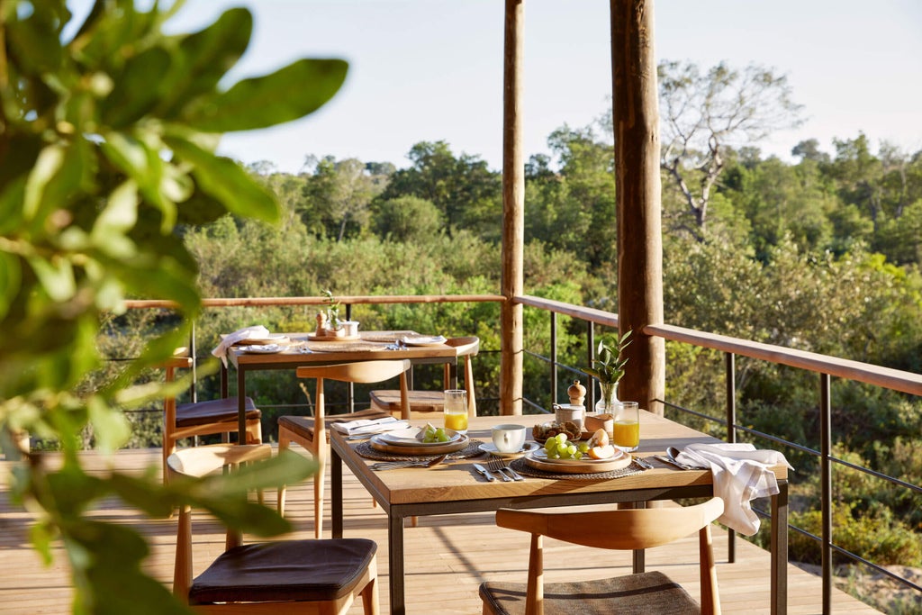 Elevated luxury safari lodge with thatched roof cottages overlooking lush African savanna at sunset, wooden deck extends over river