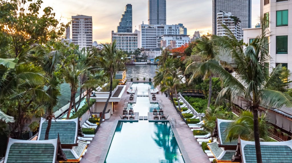 Majestic Peninsula Hotel Bangkok at sunset, reflecting in serene pool with illuminated palm trees and traditional Thai architecture