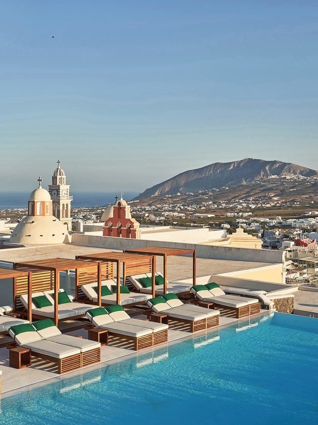 Luxurious white-washed Santorini hotel with cascading infinity pools overlooking azure Aegean Sea, traditional Cycladic architecture at sunset