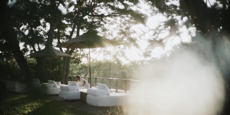 Contemporary luxury hotel suite with private balcony overlooking lush Balinese jungle, featuring traditional stone architecture and infinity pool