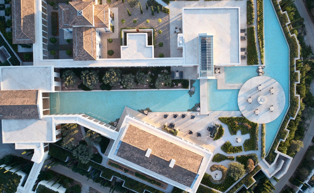 Grecian luxury resort featuring infinity pool overlooking Aegean Sea, surrounded by stone columns and modern architecture at sunset