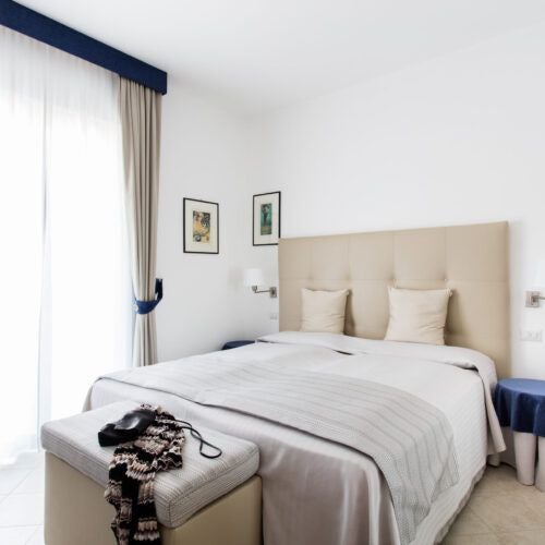 Elegant Italian villa bedroom with minimalist design, soft neutral tones, contemporary furnishings, and panoramic scenic view of landscaped gardens and rolling countryside