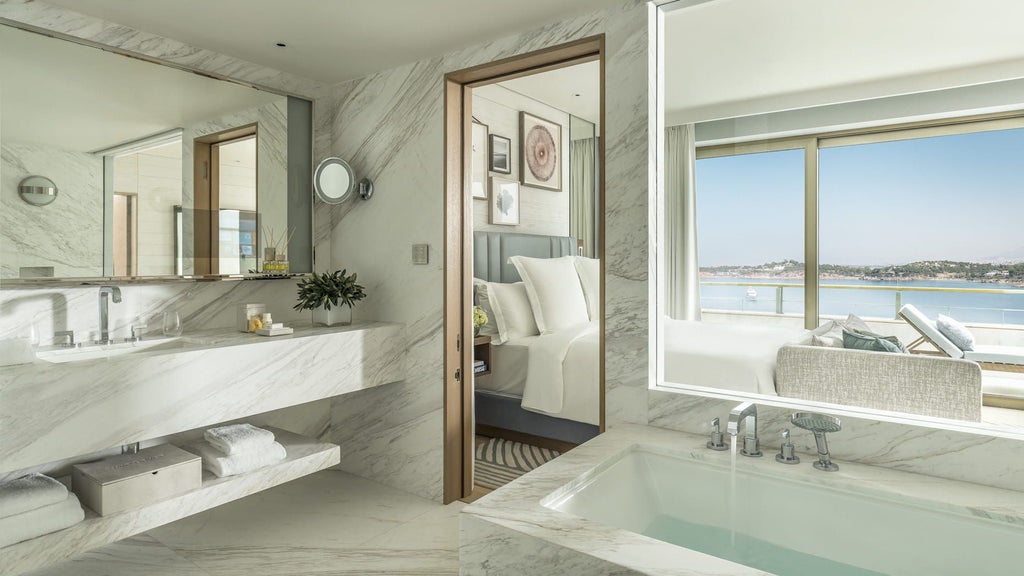 Elegant hotel suite with floor-to-ceiling windows overlooking the Aegean Sea, featuring modern furnishings and a private terrace lounge area