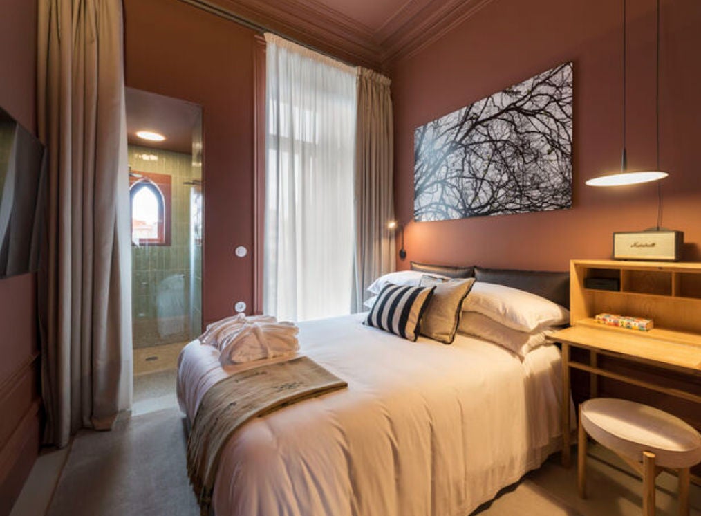 Elegant hotel room with white-draped double bed, antique wooden furniture, floor-to-ceiling windows and traditional Portuguese decor