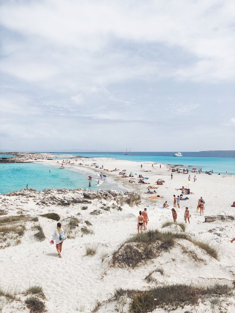 Crystal-clear turquoise waters meet pristine white sand beach on Formentera island, with luxury yachts anchored along the Mediterranean horizon