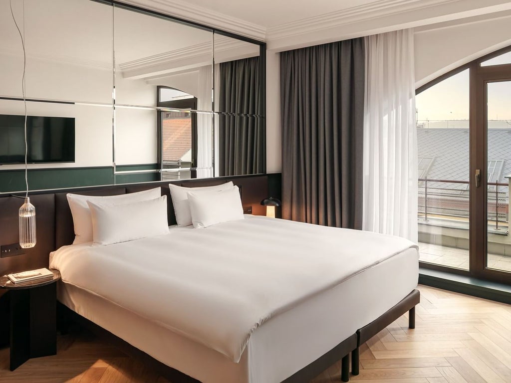 Elegant executive suite at Almanac X Alcron Prague with plush king bed, modern furniture, and private balcony overlooking city's sophisticated urban landscape