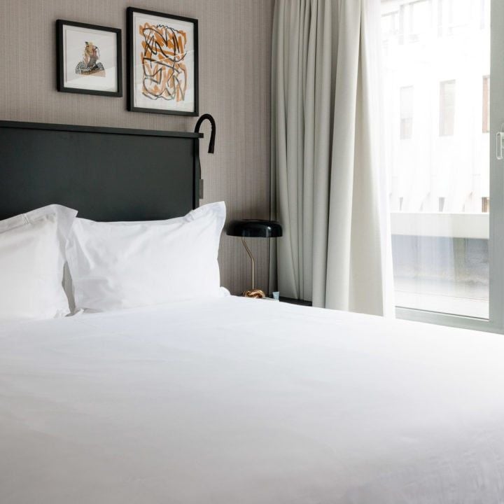 Spacious grand luxury hotel room with plush white bedding, elegant furnishings, city view, and modern Belgian design in Brussels city center