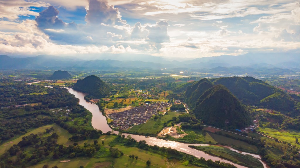 Two ancient stone pagodas on mountain peak among lush greenery, with distant misty mountains creating serene Thai landscape