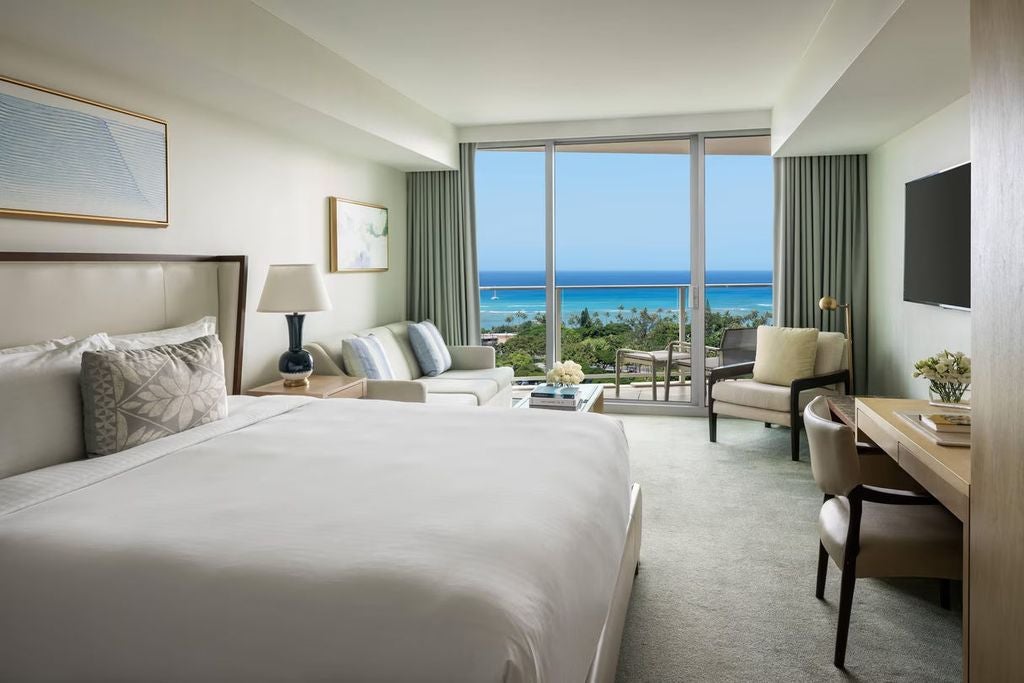 Modern high-rise hotel with glass facade, ocean-view balconies, and palm-lined infinity pool overlooking Waikiki Beach at sunset