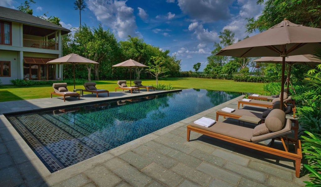 Luxury resort villa with infinity pool overlooking tropical gardens and Mekong River, featuring modern Vietnamese architecture at sunset