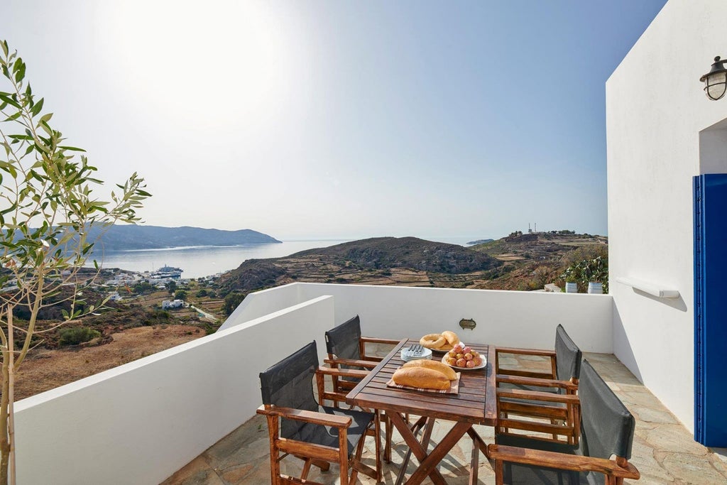 Mediterranean stone villa with white-trimmed windows, terracotta roof, surrounded by lush olive grove with panoramic Aegean Sea backdrop, showcasing elegant architectural design of renowned author's residence