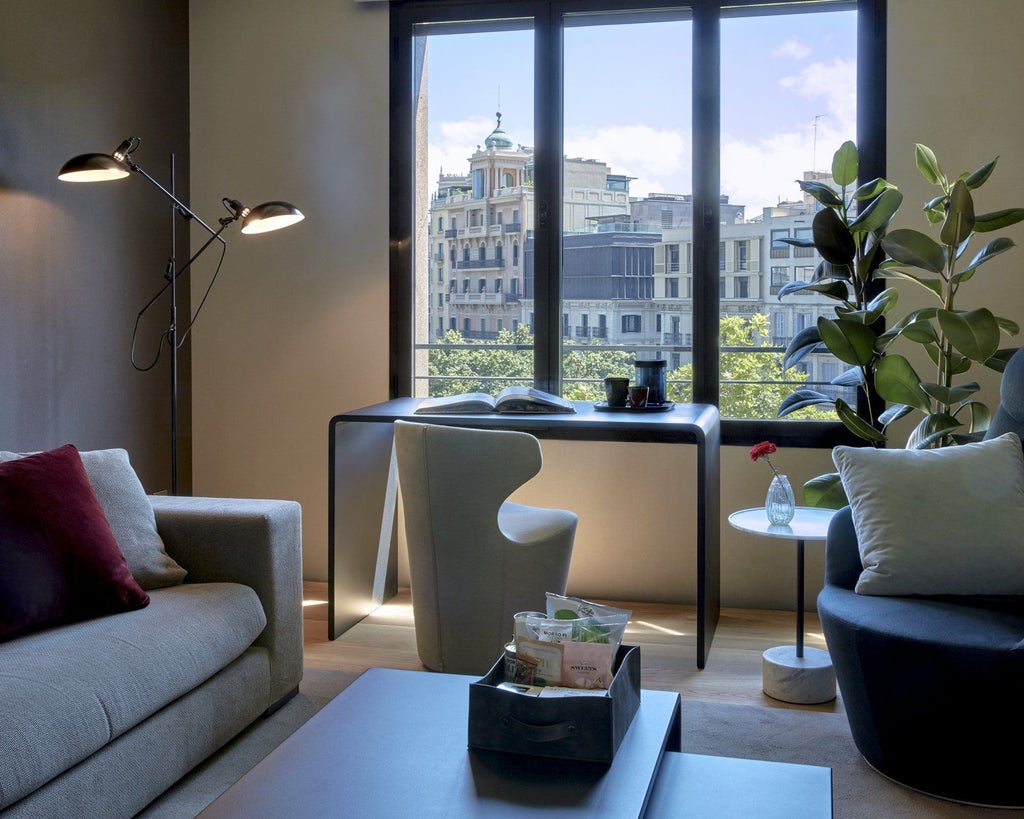 Sleek, modern Sir City Suite with panoramic urban views, minimalist design, king bed, contemporary furnishings, and floor-to-ceiling windows overlooking Spanish cityscape