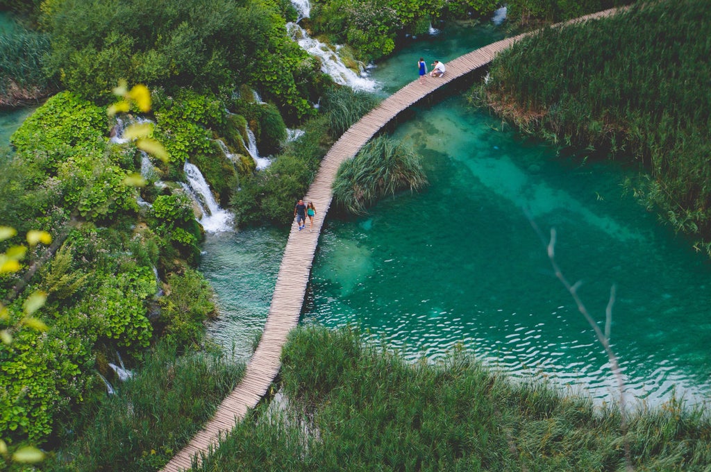 Turquoise waterfalls cascade between wooden walkways through lush forest at Croatia's Plitvice Lakes, reflecting in crystal-clear pools