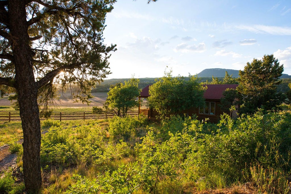 Rustic luxury cabin suite with wooden furnishings, soft neutral bedding, and panoramic mountain views of a scenic western landscape at Scenset Mountain Ranch.