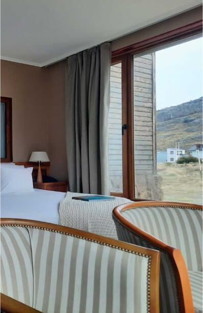 Elegant mountain-view room at Los Cerros Boutique Hotel with rustic wooden furnishings, plush bedding, and expansive windows overlooking scenic Argentinian landscape