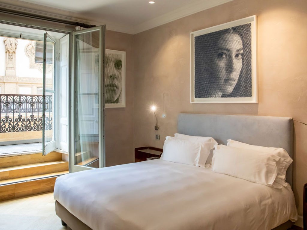 Elegant deluxe hotel room with modern Italian design, sleek furnishings, and panoramic city views of Milan's urban landscape through large windows.