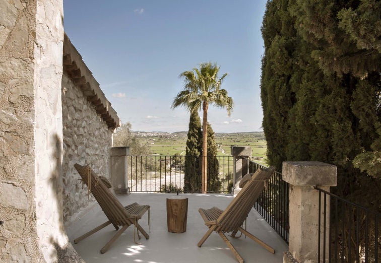 Elegant garden suite with rustic stone walls, expansive windows overlooking Mediterranean greenery, crisp white linens and modern decor