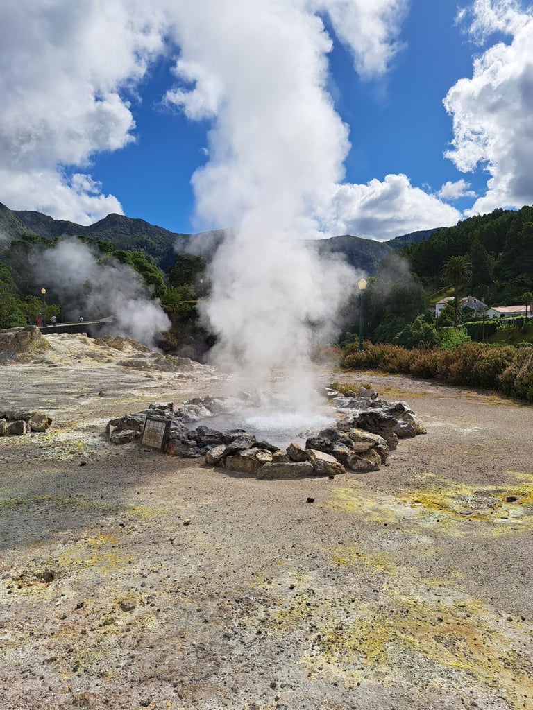 Lush green Furnas Valley with steaming volcanic hot springs, traditional stone buildings, and misty landscape in São Miguel, Azores, Portugal